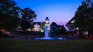 A historic building with a clock tower, surrounded by a fountain and trees.