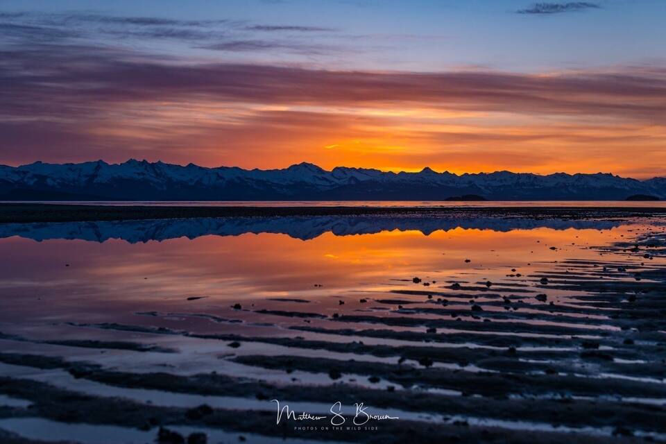 A sunset over a mountain range reflected in a calm lake.