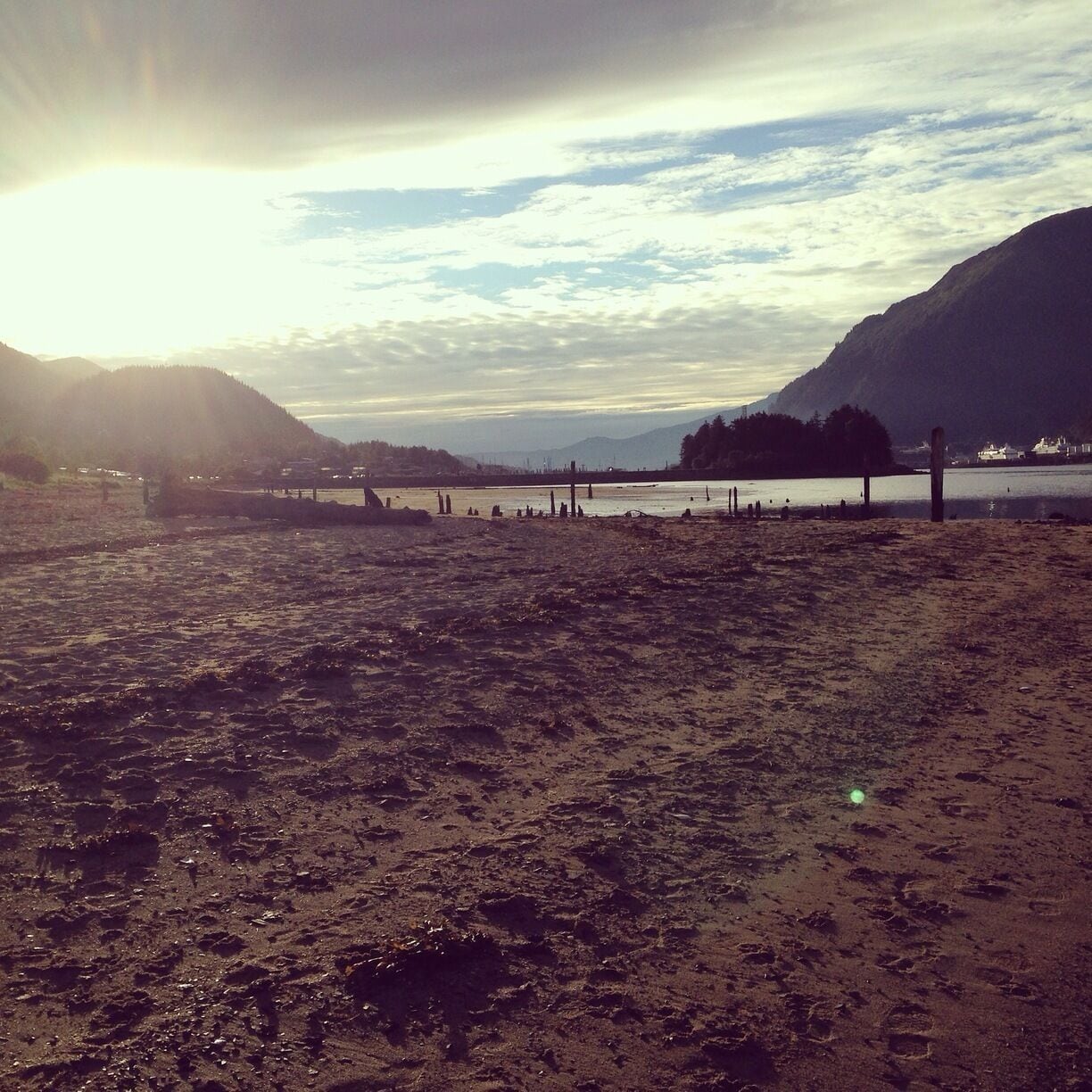 A beach with a sunset, mountains, and a calm lake.