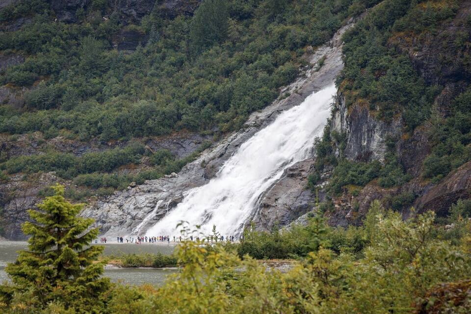 Une cascade se déversant le long d’une falaise rocheuse, entourée d’une forêt dense.