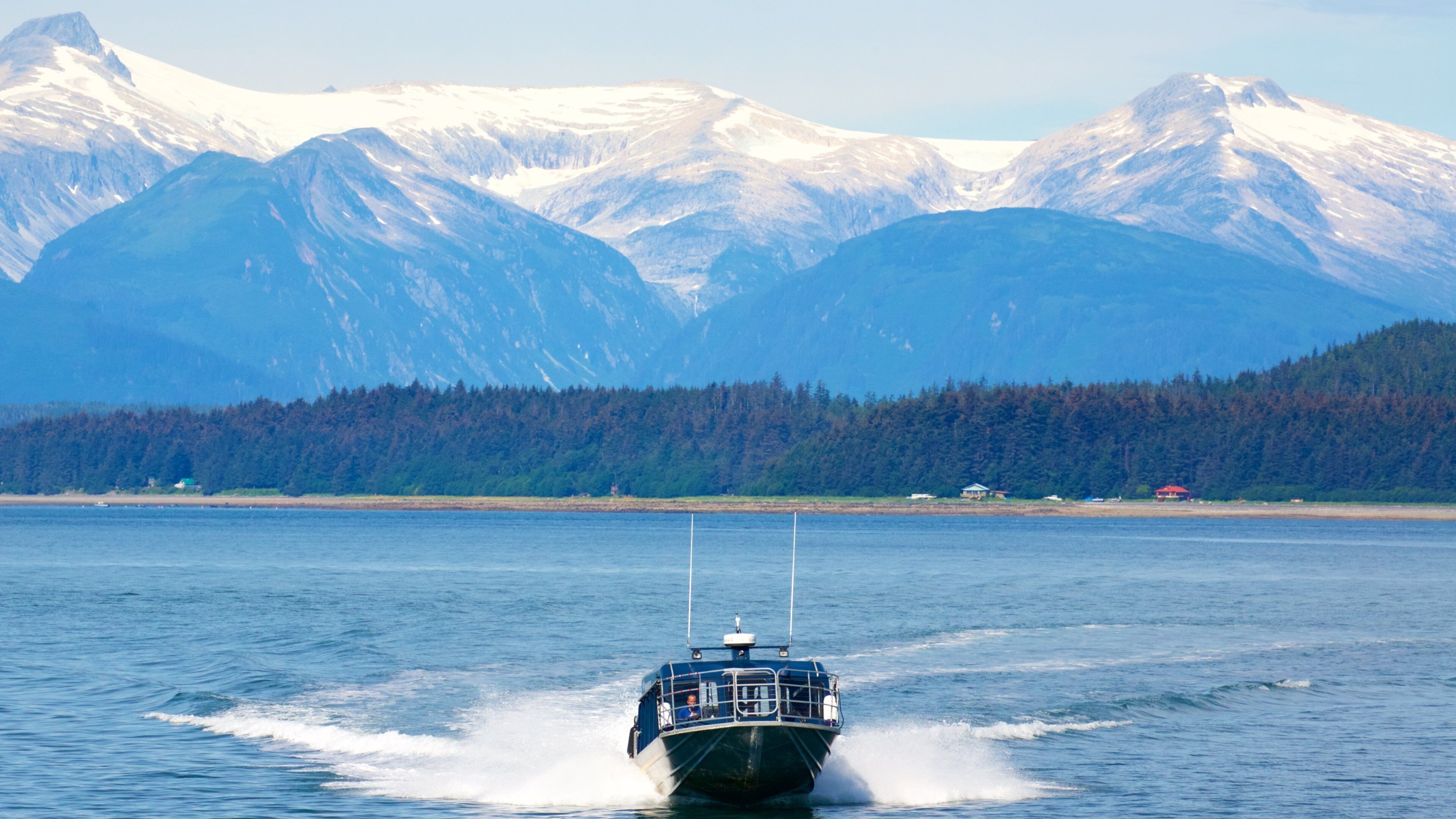 A boat moving across a calm body of water with snow-capped mountains in the background.
