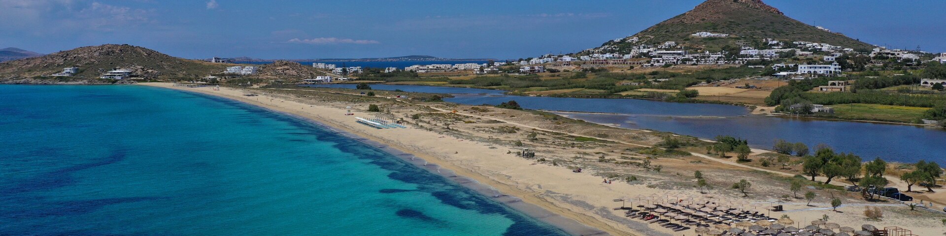 Un paisaje costero con una playa, aguas turquesas cristalinas y una colina con edificios.