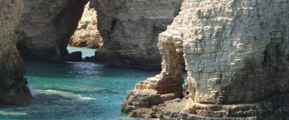 A coastal rock formation with a natural archway and clear turquoise waters.