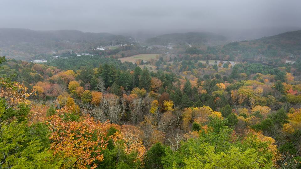 A mountainous landscape with autumn foliage, a valley, and distant buildings.