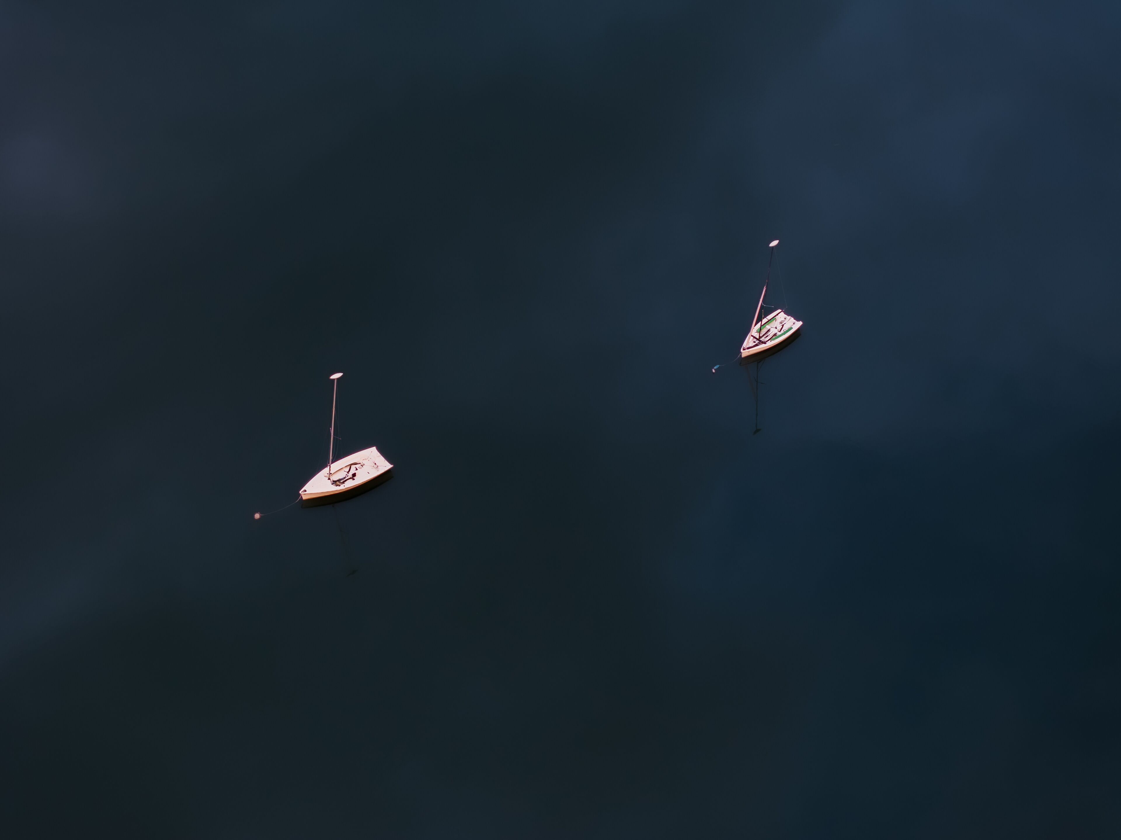 Aerial view of two sailboats floating serenely on the dark, rippled water, their white hulls contrasting against the deep blue, Boston, Massachusetts, United States.