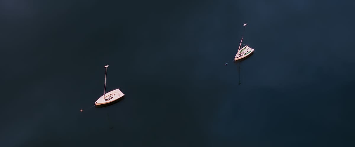 Aerial view of two sailboats floating serenely on the dark, rippled water, their white hulls contrasting against the deep blue, Boston, Massachusetts, United States.