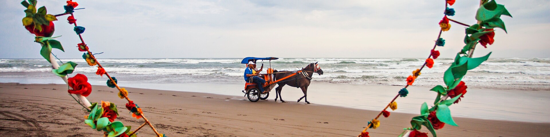 Uma praia com uma carruagem puxada a cavalo e um arranjo floral em formato de coração formando a inscrição 'PARANG TRITIS'.