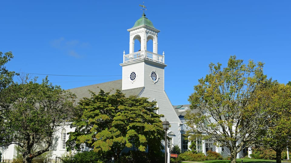 A church with a bell tower, surrounded by trees and a clear blue sky.