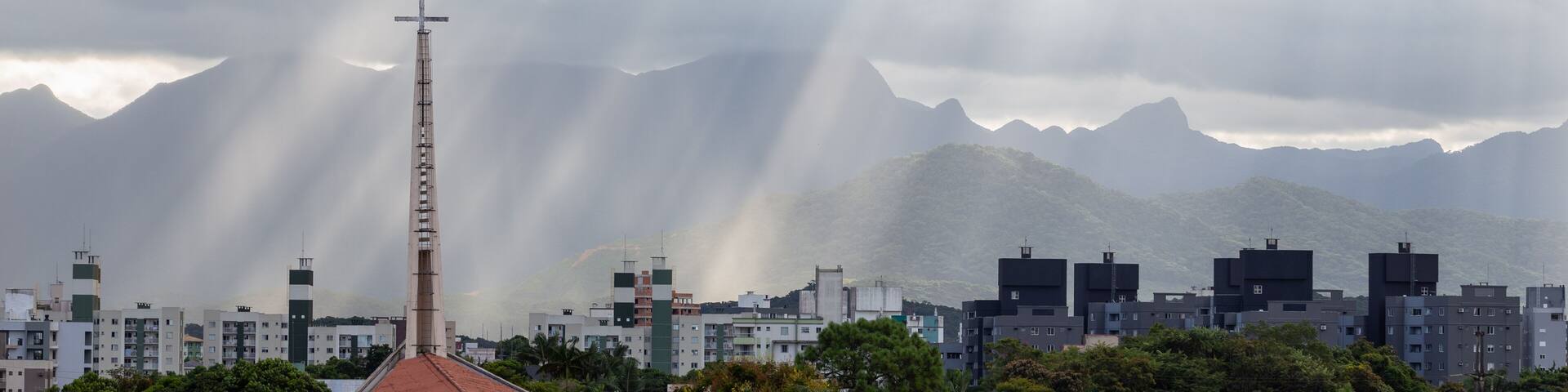 Raios de Sol passando pelas nuvens de um céu nublado em um dia chuvoso. Igreja em primeiro plano.