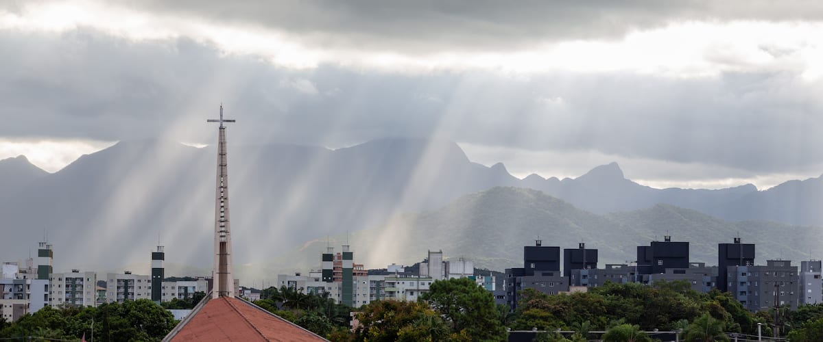 A cityscape with a prominent tower, mountains, and a cloudy sky.