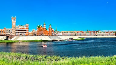 A river with a bridge, a castle-like building, and a row of colorful houses along the riverbank.