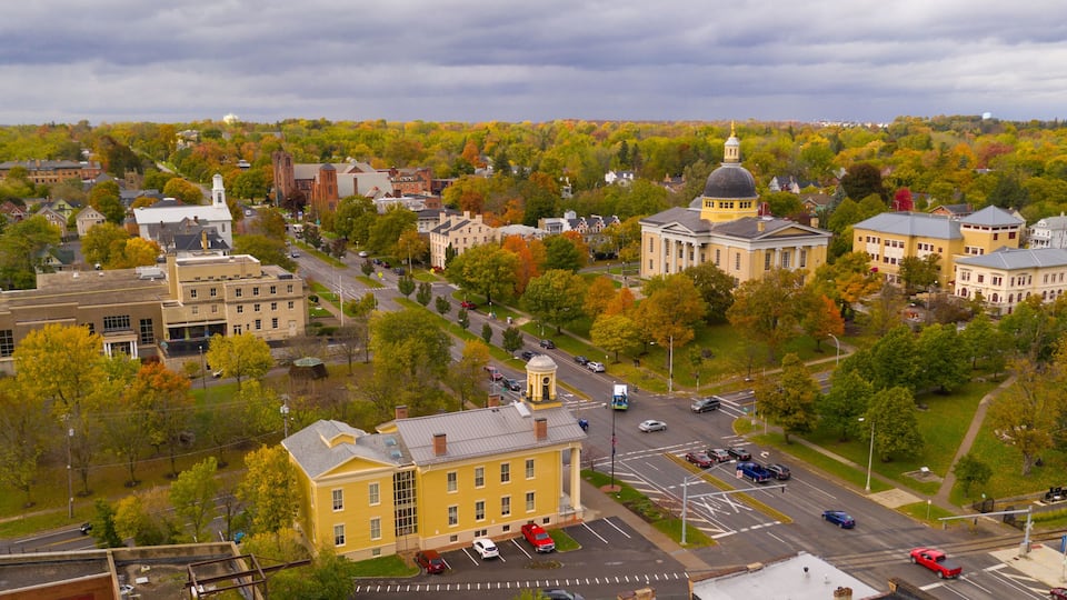 An aerial view of a town with historic buildings, a prominent yellow building, and autumn-colored trees.