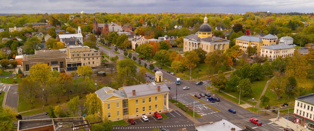 An aerial view of a town with historic buildings, a prominent yellow building, and autumn-colored trees.