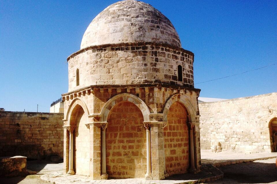 A stone dome structure with arched doorways, set against a clear blue sky.