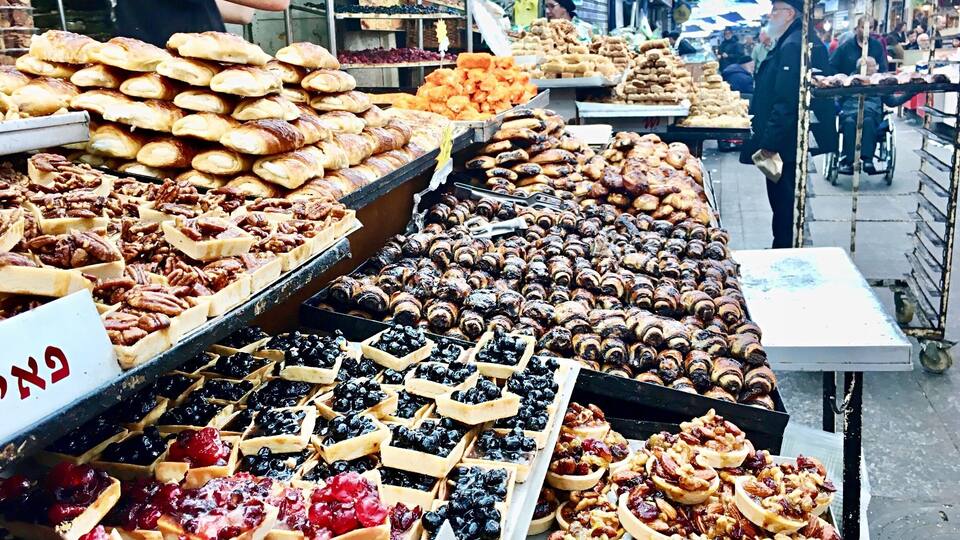 A street market with various baked goods like pastries, tarts, and pies displayed on tables.