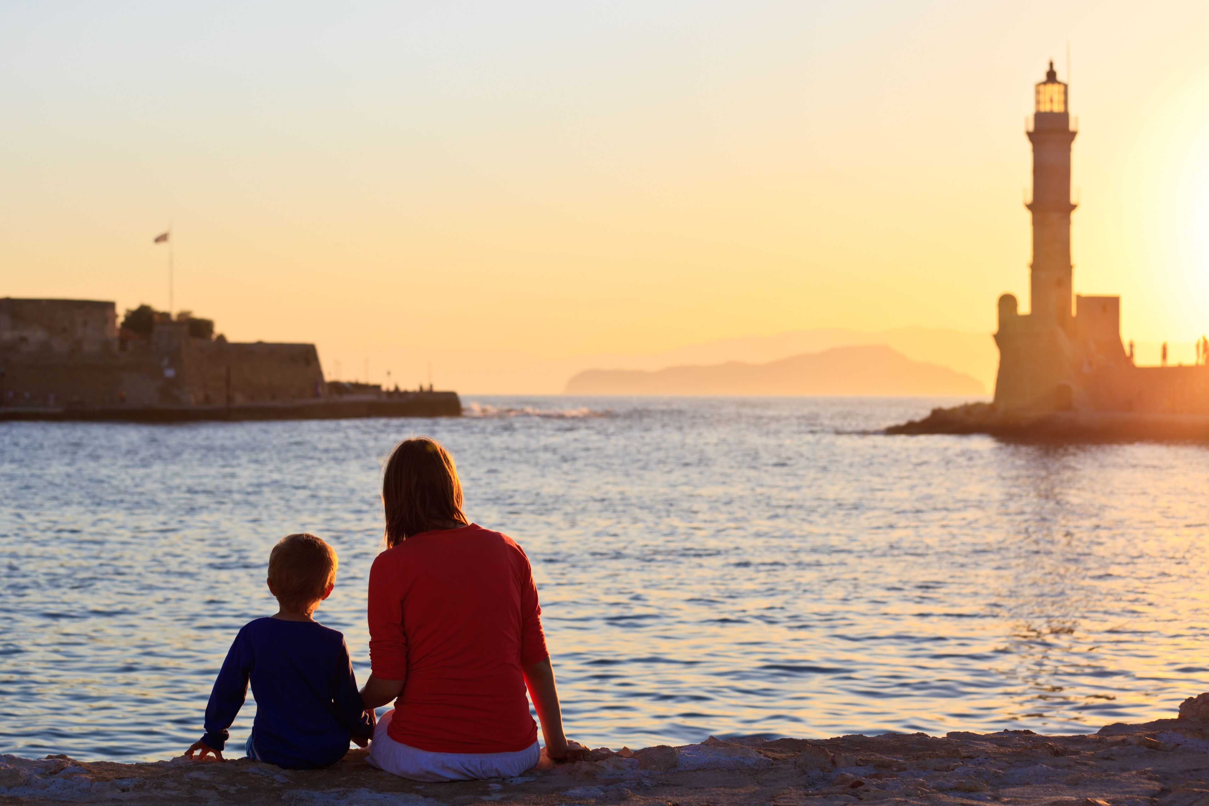 A sunset over a body of water with a lighthouse and a fortified structure in the background.