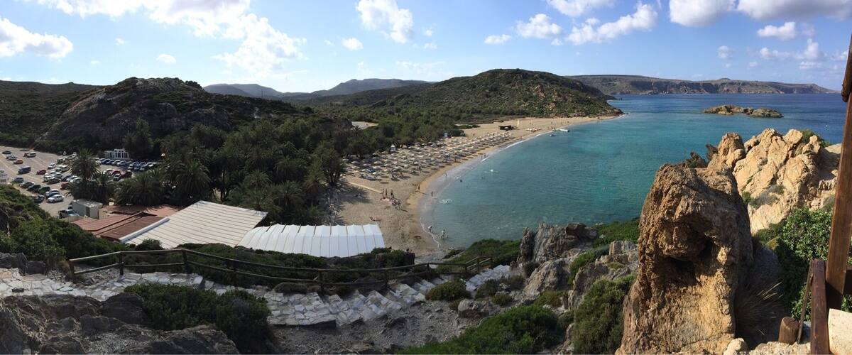 A coastal landscape with a beach, parking area, and rocky cliffs.