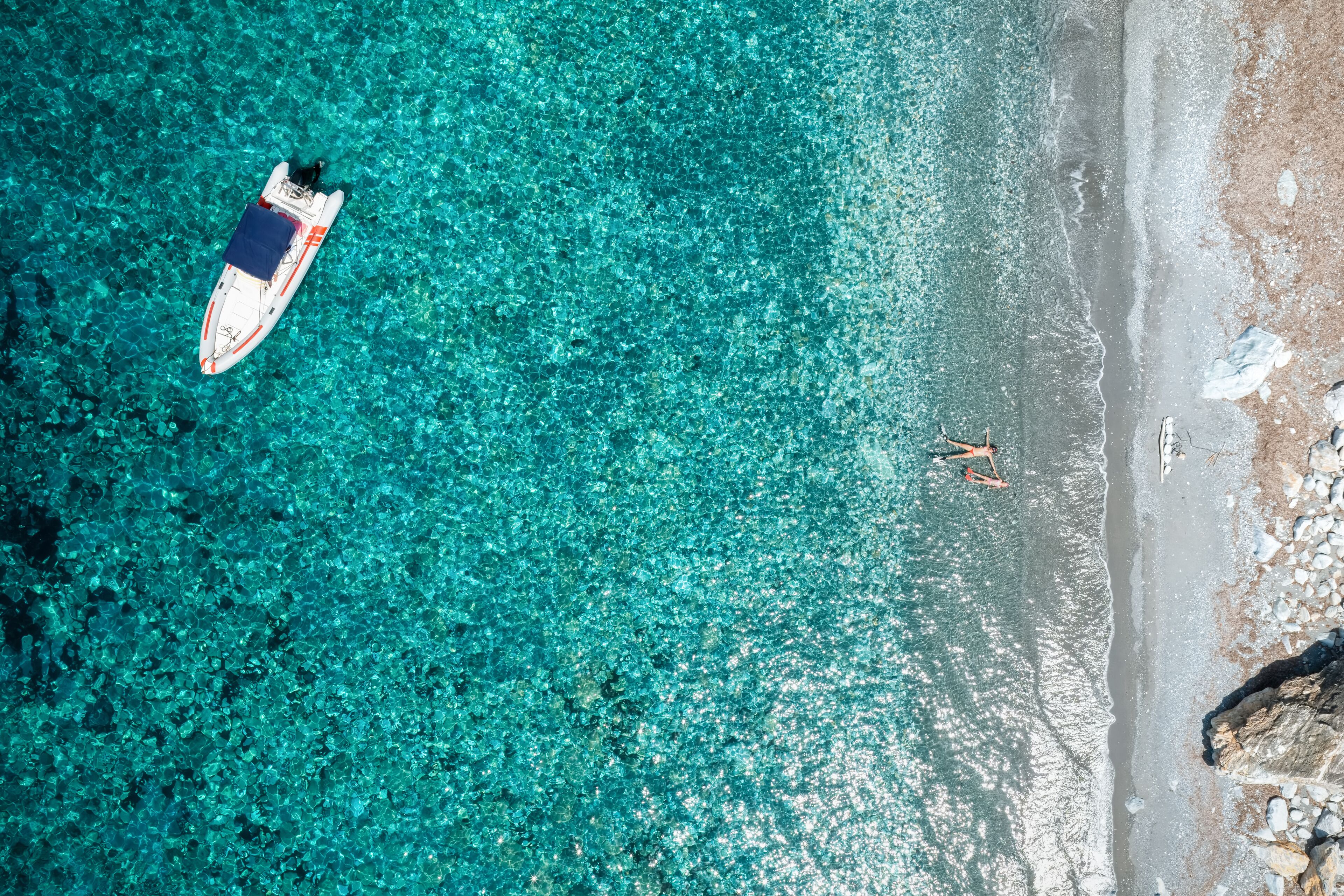 A boat on clear turquoise water, a sandy beach, and a rocky outcrop.
