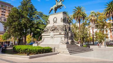 A statue of a man on a horse in a public square with palm trees and buildings in the background.