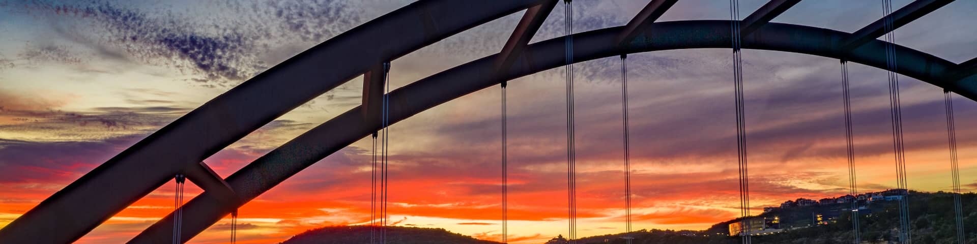 A bridge with a curved arch over a river at sunset.