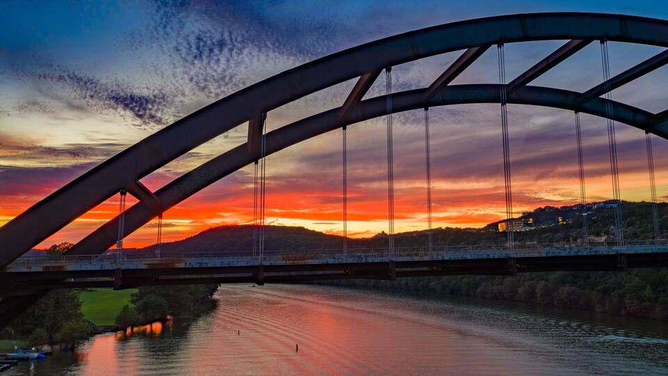 A bridge with a curved arch over a river at sunset.