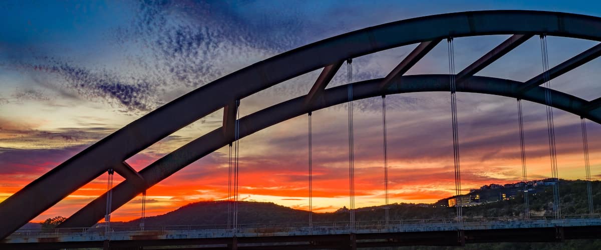 A bridge with a curved arch over a river at sunset.