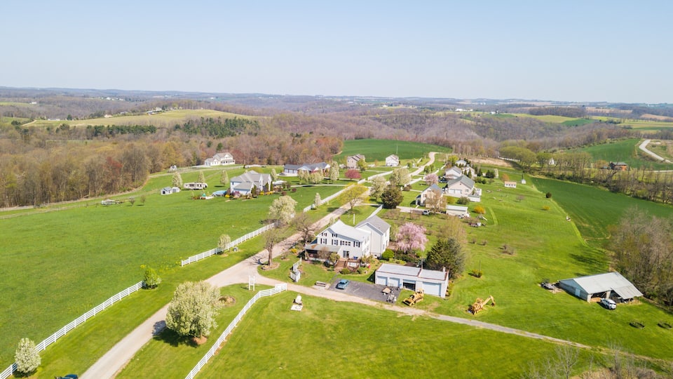 An aerial view of a rural area with green fields, a white fence, and several houses.