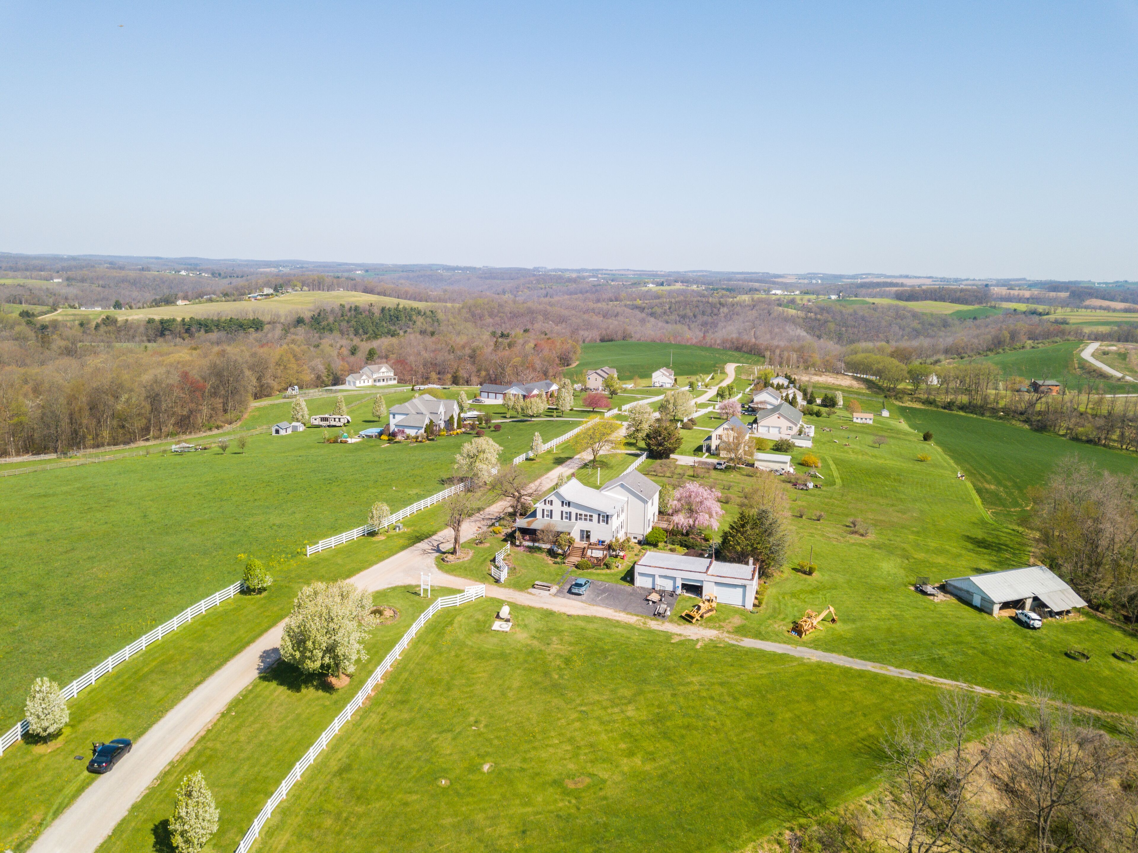 An aerial view of a rural area with green fields, a white fence, and several houses.