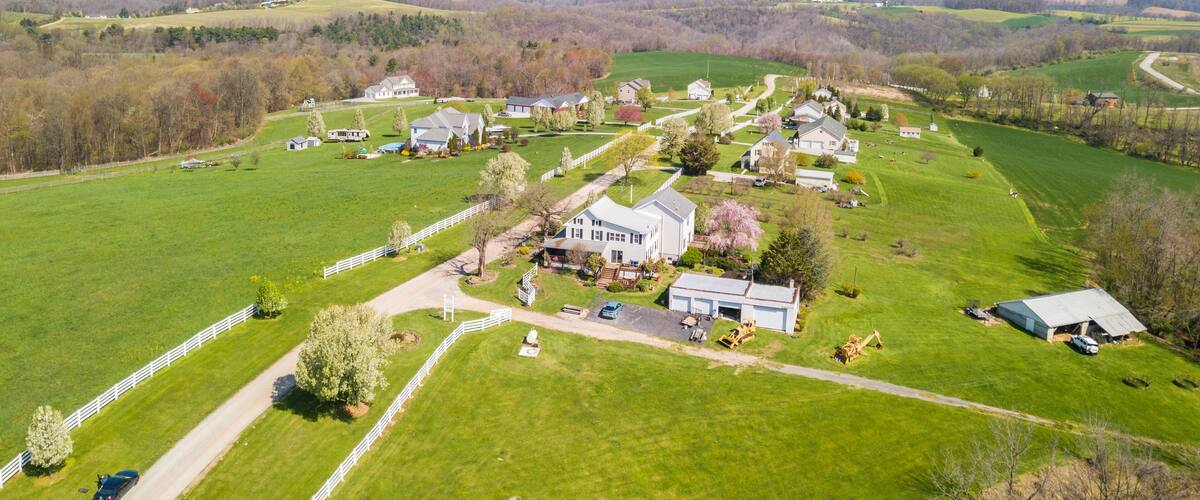 An aerial view of a rural area with green fields, a white fence, and several houses.