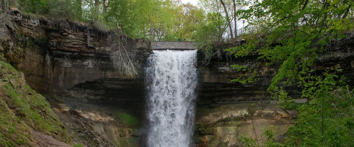 A waterfall cascading down a rocky cliff into a river surrounded by lush greenery.