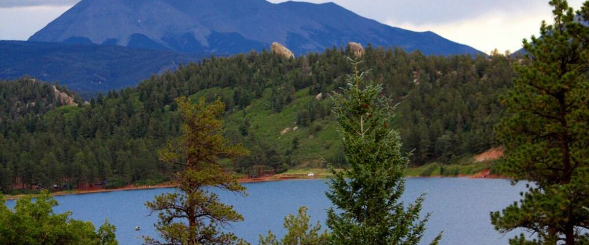 A lake surrounded by dense forest and mountains under cloudy skies.