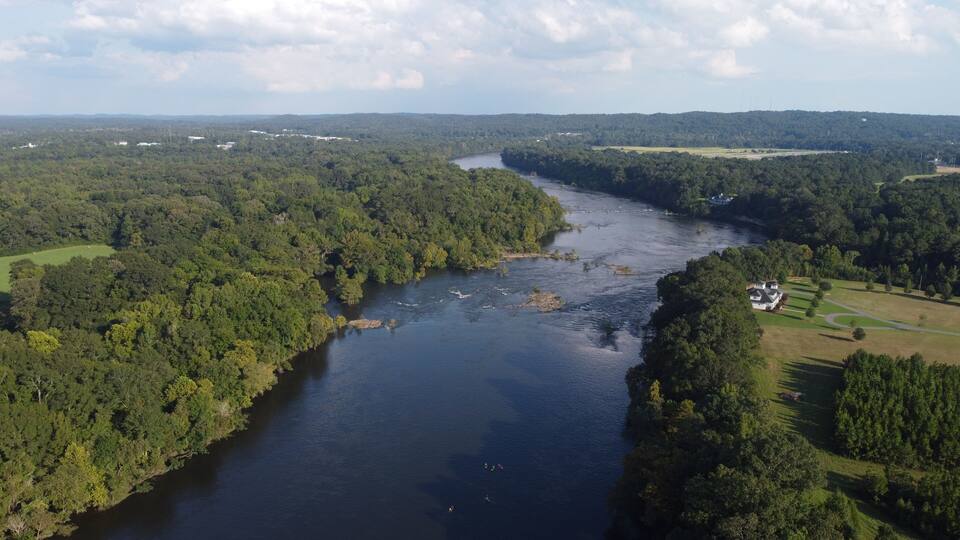 A river winding through a densely forested landscape with a small house on the right bank.
