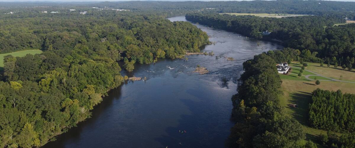 A river winding through a densely forested landscape with a small house on the right bank.