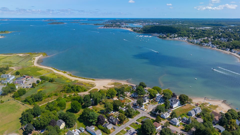 An aerial view of a coastal town with a marina, residential areas, and a large body of water.