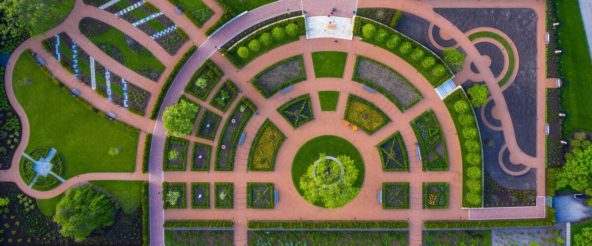 An aerial view of a landscaped park with winding paths, a central circular garden, and a fountain.
