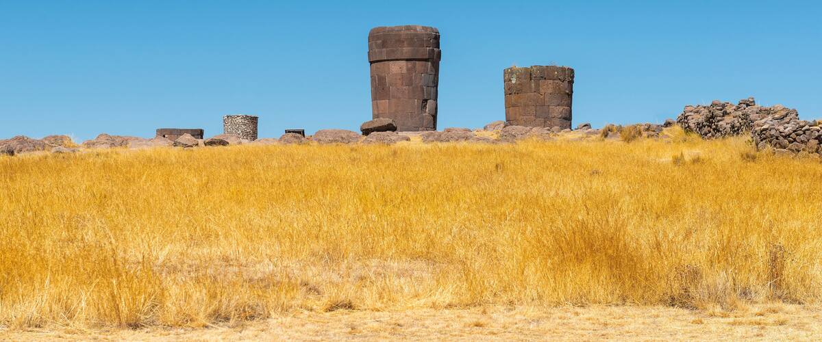 A clear blue sky, a large field of dry grass, and several stone structures.