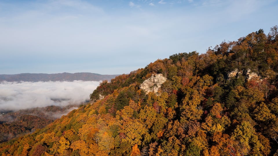 A mountainous landscape with autumn foliage, a rocky outcrop, and a valley below shrouded in clouds.