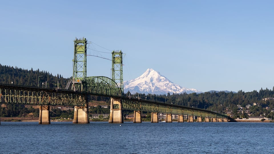 A long bridge spanning a river with a mountain in the background.