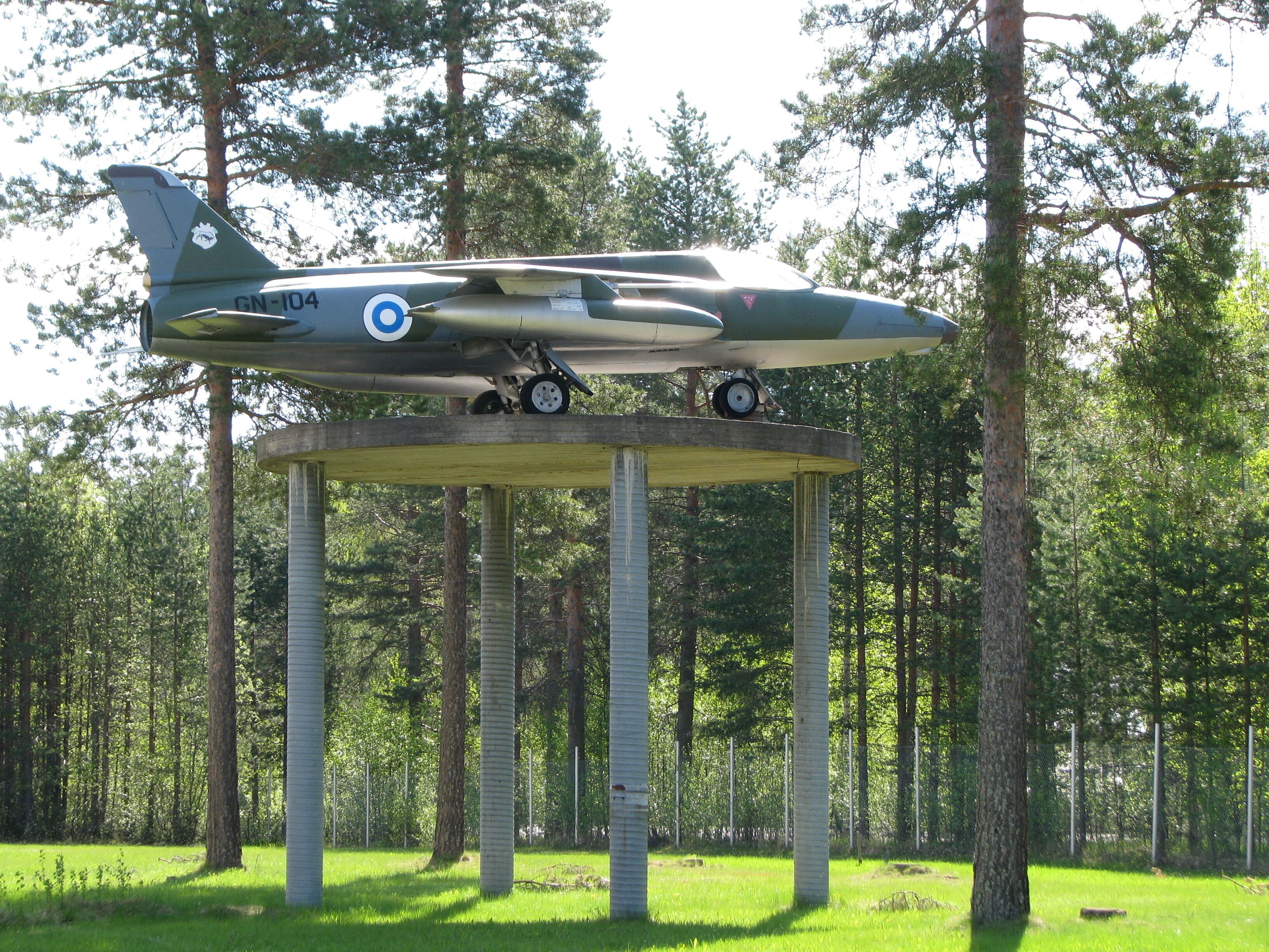 A military aircraft on a concrete platform in a forest.