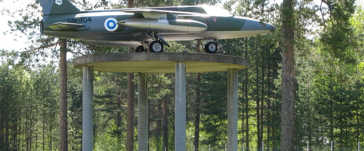 A military aircraft on a concrete platform in a forest.