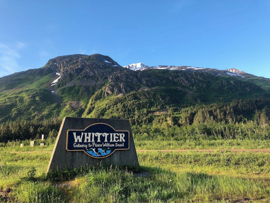 A sign reading "Whittier Gateway to Prince William Sound" with a mountainous backdrop.