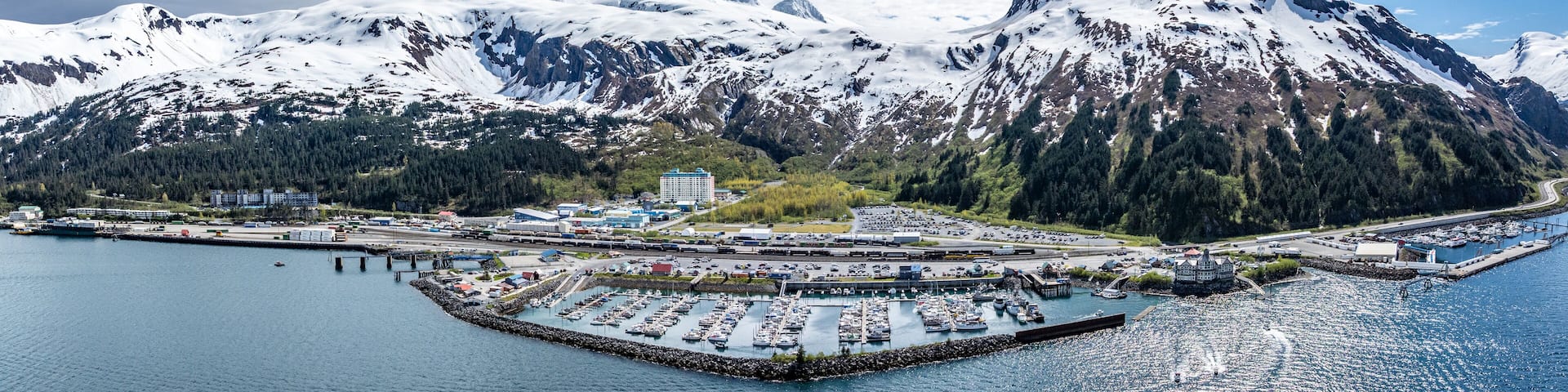 wide angle panoramic aerial landscape view of Whittier Cityscape with Harbor and Port located at head of Passage Canal in Alaska, USA, with snow covered mountain landscape in background