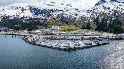 wide angle panoramic aerial landscape view of Whittier Cityscape with Harbor and Port located at head of Passage Canal in Alaska, USA, with snow covered mountain landscape in background