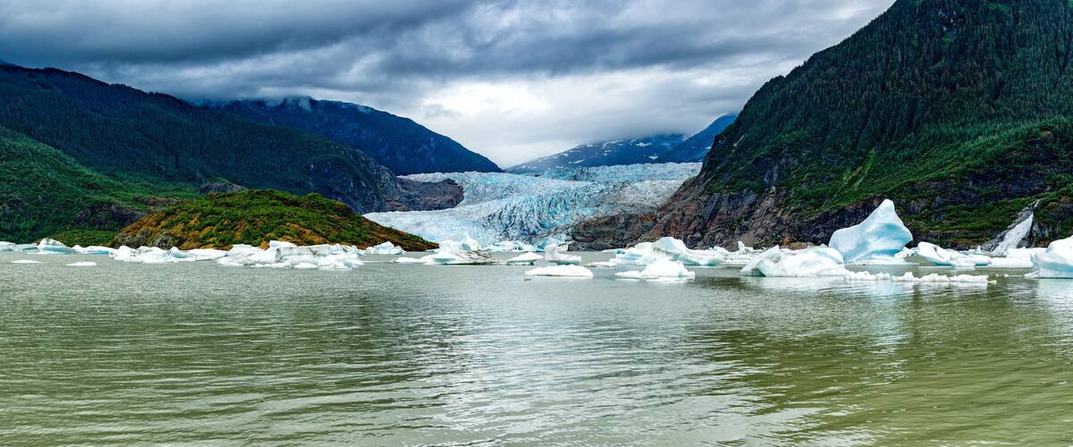 A glacier with icebergs in a valley surrounded by mountains.