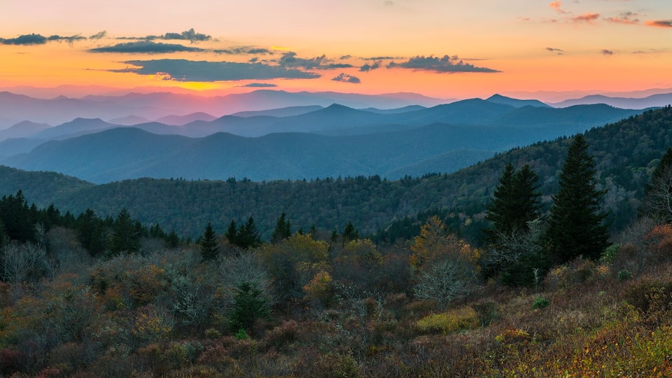 A mountainous landscape with dense forests and a sunset sky.
