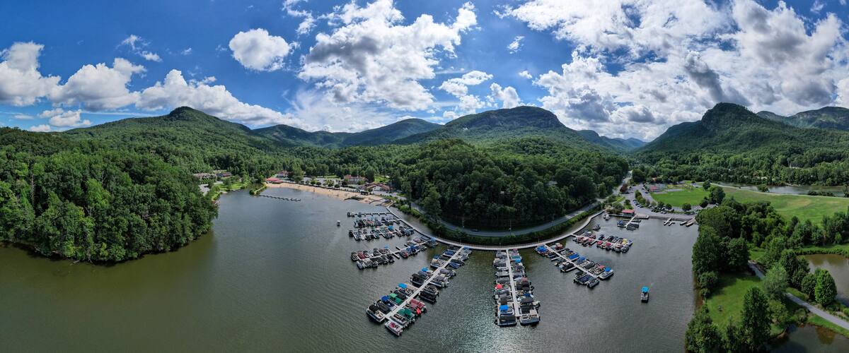 A river with a marina surrounded by lush green hills and mountains under a partly cloudy sky.