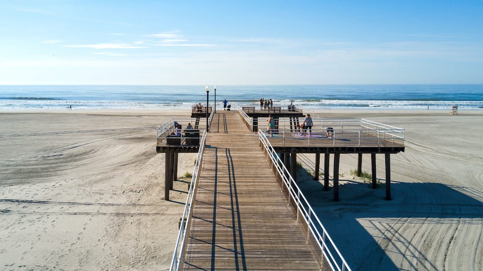 A wooden pier extending into the ocean with people on it and a clear sky above.
