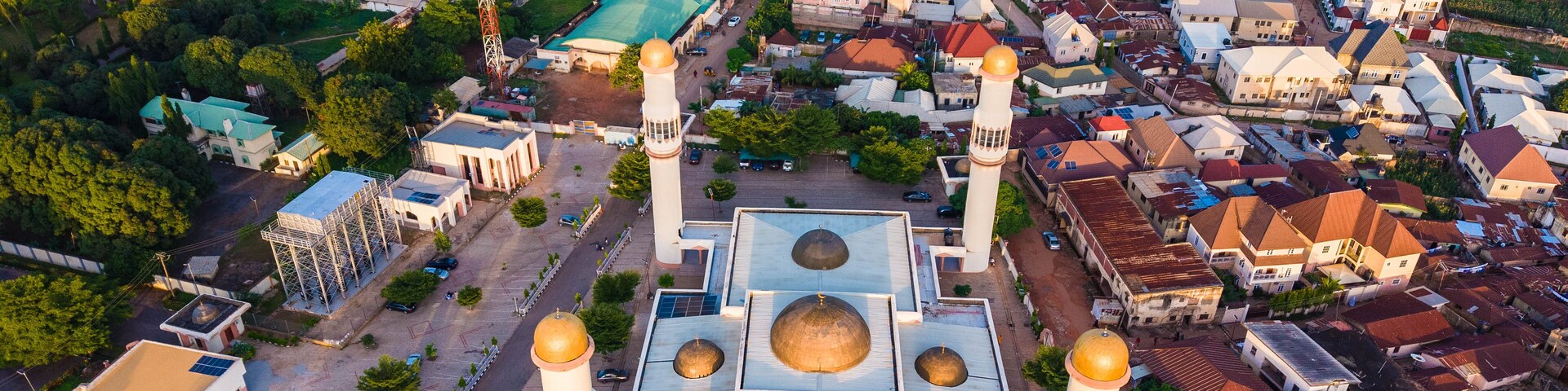 Vista aérea de una mezquita con cuatro cúpulas doradas y dos minaretes, rodeada de edificios residenciales y vegetación.
