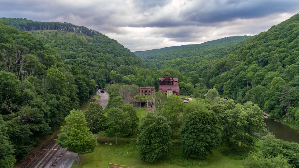 A lush green valley with a red-roofed building surrounded by dense forest and a river.