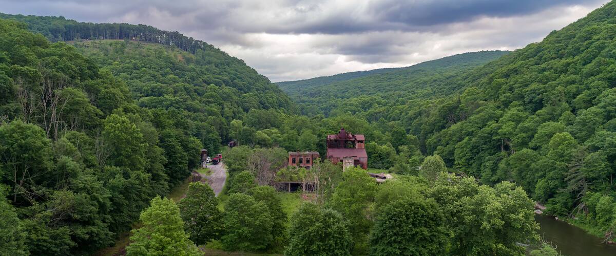 A lush green valley with a red-roofed building surrounded by dense forest and a river.